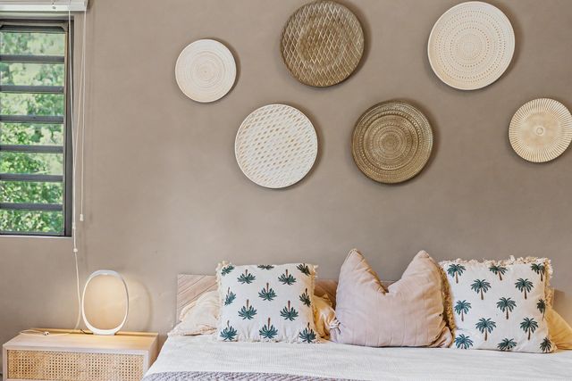 Bed styled with palm-print cushions beneath woven wall baskets